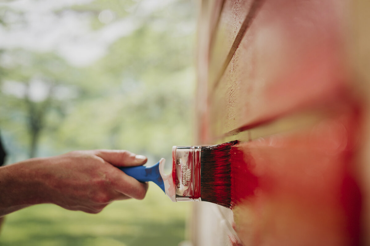 Ulkomaalaus Kuvassa on pensselillä punaista seinää maalaava käsi.